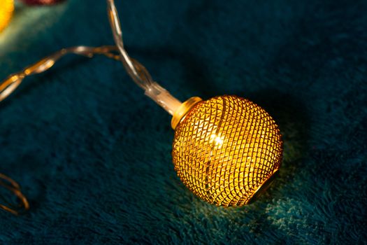 Battery garland with metallic grid balls on blue blanket. Closeup view with blurred background.