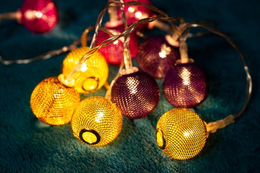 Battery garland with metallic grid balls on blue blanket. Closeup view with blurred background.