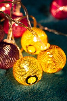Battery garland with metallic grid balls on blue blanket. Closeup view with blurred background.