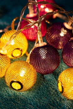 Battery garland with metallic grid balls on blue blanket. Closeup view with blurred background.