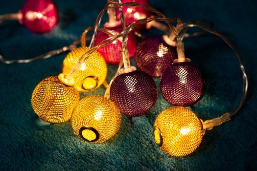 Battery garland with metallic grid balls on blue blanket. Closeup view with blurred background.