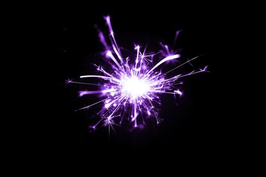Low light photo of bengali fire isolated on black background with purple toning. A lot of light and sparks. Underexposed photo.