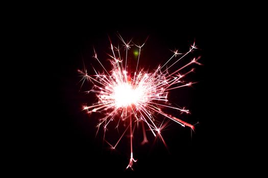 Low light photo of bengali fire isolated on black background with red toning. A lot of light and sparks. Underexposed photo.