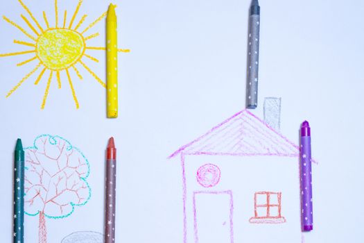 Children`s drawing of house, tree, sun and rock on white paper with wax pencils. Kindergarten age drawings.
