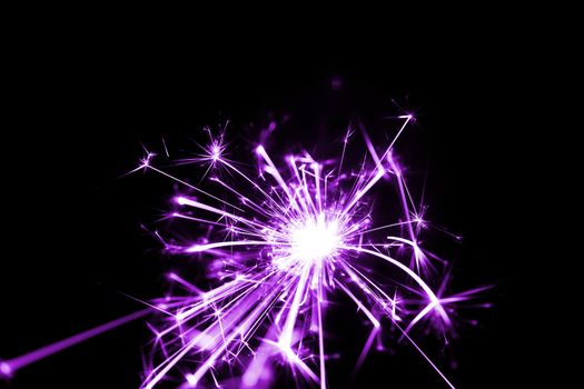 Low light photo of bengali fire isolated on black background with purple toning. A lot of light and sparks. Underexposed photo.
