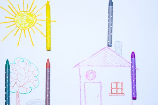 Children`s drawing of house, tree, sun and rock on white paper with wax pencils. Kindergarten age drawings.