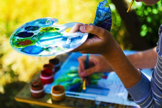 Young artist man drawing outdoors with palette in hand.
