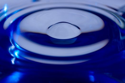 Waves on water surface in blue glass. Drop falling and splashing in water. Soft focus photo.