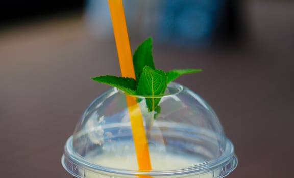 Pina colada cocktail in plactic glass with cover and tubule. Mint leaf on cover. Close-up view.