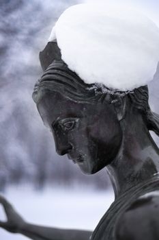 Bronze monument of a woman in winter snow park. Closeup with blurred background.