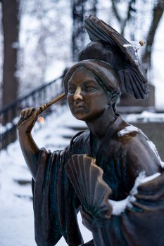 Bronze monument of a chinese old man with umbrella in winter snow park. Closeup with blurred background.