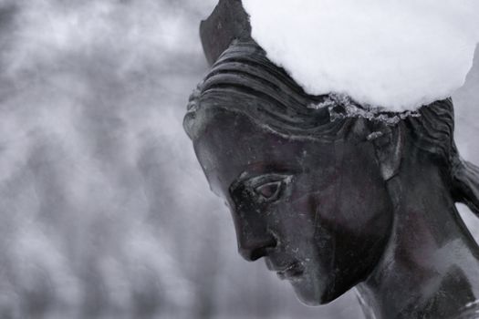 Bronze monument of a woman in winter snow park. Closeup with blurred background.