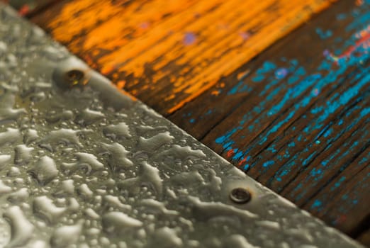 The metal sheet on the left and the boards are orange and blue on the right. Rain drops on metal and wood. The photo shows a part of a children's hill