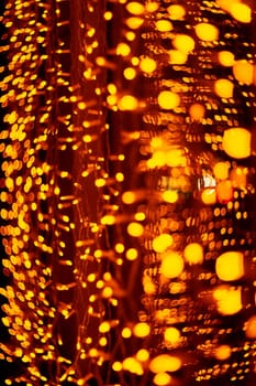 Vertical Christmas garland wall on glass window. Light is orange and defocused. Blurred background, new year mood.