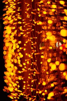 Vertical Christmas garland wall on glass window. Light is orange and defocused. Blurred background, new year mood.