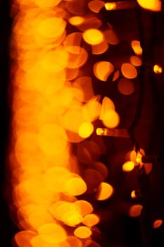 Vertical Christmas garland wall on glass window. Light is orange and defocused. Blurred background, new year mood.