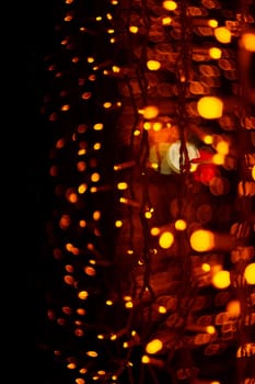 Vertical Christmas garland wall on glass window. Light is orange and defocused. Blurred background, new year mood.