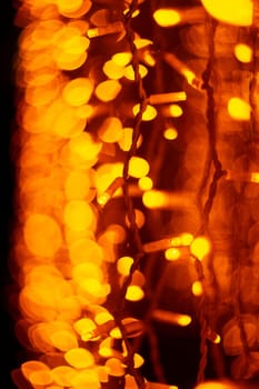Vertical Christmas garland wall on glass window. Light is orange and defocused. Blurred background, new year mood.