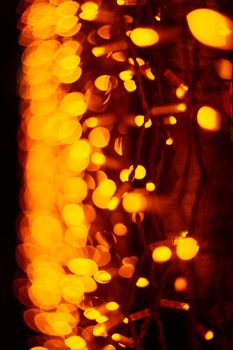Vertical Christmas garland wall on glass window. Light is orange and defocused. Blurred background, new year mood.