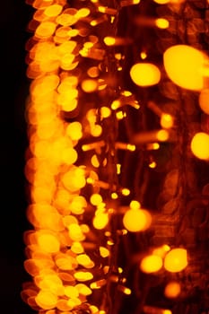 Vertical Christmas garland wall on glass window. Light is orange and defocused. Blurred background, new year mood.