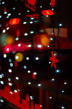 Vertical Christmas garland wall on glass window. Light is white and defocused. Blurred background, new year mood.