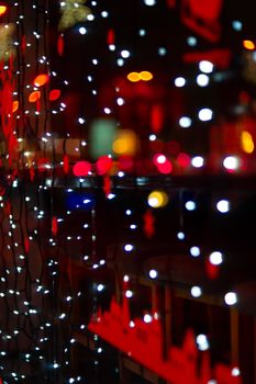 Vertical Christmas garland wall on glass window. Light is white and defocused. Blurred background, new year mood.