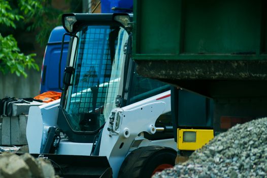 a pile of rubble and soil in the foreground. in the background a mini bulldozer loader and a truck