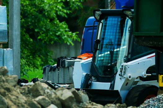 a pile of rubble and soil in the foreground. in the background a mini bulldozer loader and a truck