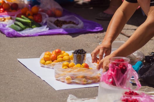 Street spontaneous mart on the asphalt. An old woman straightens vegetables on white cloth.