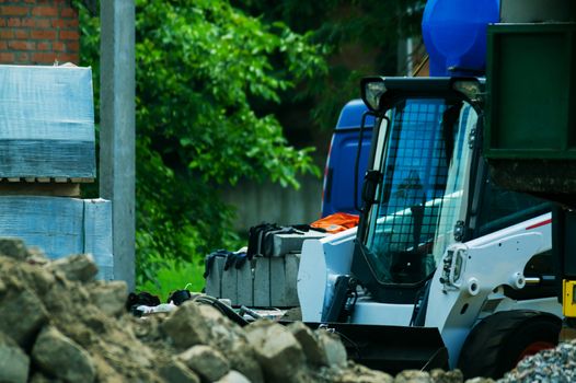 a pile of rubble and soil in the foreground. in the background a mini bulldozer loader and a truck