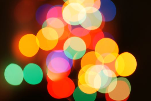 Multi-color holiday garland. Garland is blurred. Many colorful round lights. Fully defocused photo. Blurred background and foreground. Holiday mood. New Year and Christmas is coming.