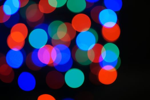 Multi-color blue holiday garland. Garland is blurred. Many big colorful round lights. Fully defocused photo. Blurred background and foreground. Holiday mood. New Year and Christmas is coming.
