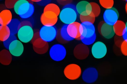Multi-color blue holiday garland. Garland is blurred. Many big colorful round lights. Fully defocused photo. Blurred background and foreground. Holiday mood. New Year and Christmas is coming.