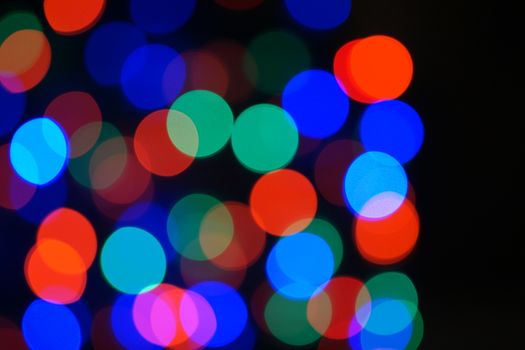 Multi-color blue holiday garland. Garland is blurred. Many big colorful round lights. Fully defocused photo. Blurred background and foreground. Holiday mood. New Year and Christmas is coming.