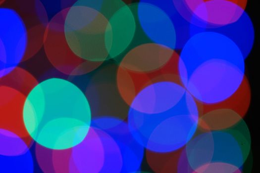 Multi-color blue holiday garland. Garland is blurred. Many very big colorful round lights. Fully defocused photo. Blurred background and foreground. Holiday mood. New Year and Christmas is coming.