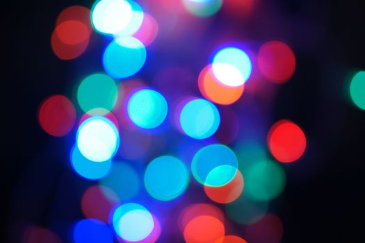 Multi-color blue holiday garland. Garland is blurred. Many big colorful round lights. Fully defocused photo. Blurred background and foreground. Holiday mood. New Year and Christmas is coming.