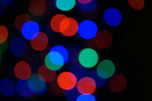Multi-color blue holiday garland. Garland is blurred. Many big colorful round lights. Fully defocused photo. Blurred background and foreground. Holiday mood. New Year and Christmas is coming.