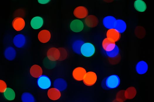 Multi-color blue holiday garland. Garland is blurred. Many big colorful round lights. Fully defocused photo. Blurred background and foreground. Holiday mood. New Year and Christmas is coming.