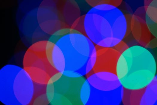 Multi-color blue holiday garland. Garland is blurred. Many very big colorful round lights. Fully defocused photo. Blurred background and foreground. Holiday mood. New Year and Christmas is coming.