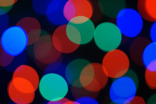 Multi-color blue holiday garland. Garland is blurred. Many big colorful round lights. Fully defocused photo. Blurred background and foreground. Holiday mood. New Year and Christmas is coming.