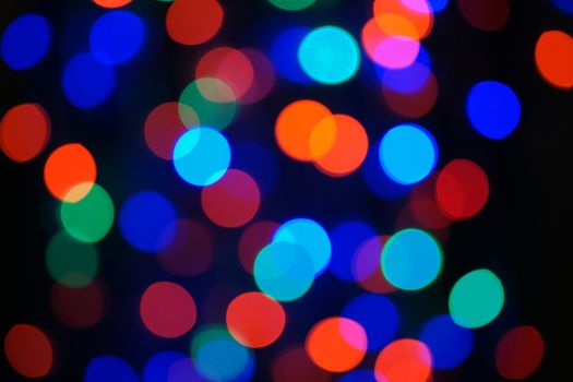 Multi-color blue holiday garland. Garland is blurred. Many big colorful round lights. Fully defocused photo. Blurred background and foreground. Holiday mood. New Year and Christmas is coming.