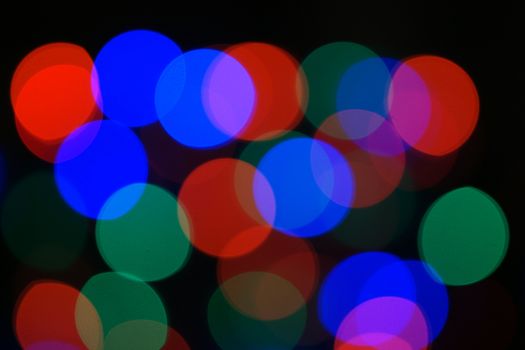 Multi-color blue holiday garland. Garland is blurred. Many big colorful round lights. Fully defocused photo. Blurred background and foreground. Holiday mood. New Year and Christmas is coming.