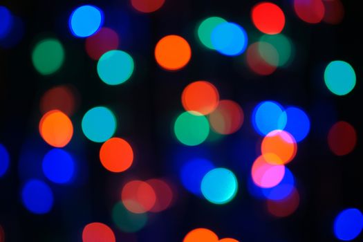Multi-color blue holiday garland. Garland is blurred. Many big colorful round lights. Fully defocused photo. Blurred background and foreground. Holiday mood. New Year and Christmas is coming.