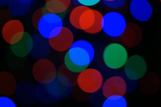 Multi-color blue holiday garland. Garland is blurred. Many big colorful round lights. Fully defocused photo. Blurred background and foreground. Holiday mood. New Year and Christmas is coming.