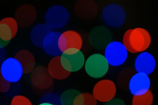 Multi-color blue holiday garland. Garland is blurred. Many big colorful round lights. Fully defocused photo. Blurred background and foreground. Holiday mood. New Year and Christmas is coming.