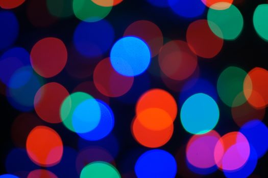 Multi-color blue holiday garland. Garland is blurred. Many big colorful round lights. Fully defocused photo. Blurred background and foreground. Holiday mood. New Year and Christmas is coming.