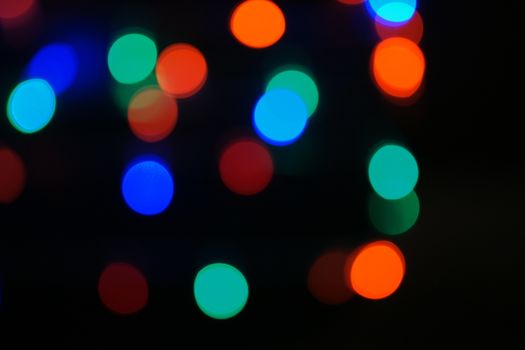 Multi-color blue holiday garland. Garland is blurred. Many big colorful round lights. Fully defocused photo. Blurred background and foreground. Holiday mood. New Year and Christmas is coming.