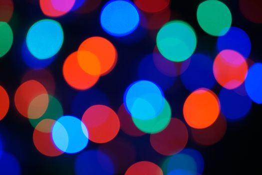 Multi-color blue holiday garland. Garland is blurred. Many big colorful round lights. Fully defocused photo. Blurred background and foreground. Holiday mood. New Year and Christmas is coming.