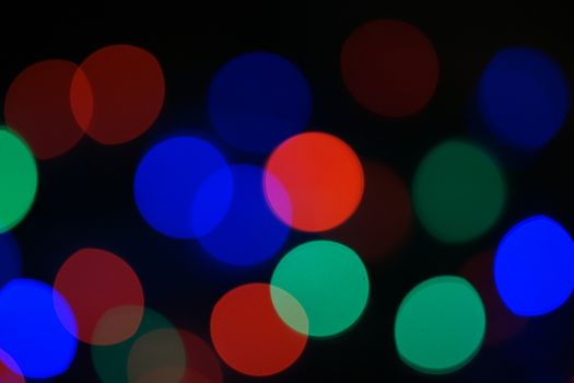 Multi-color blue holiday garland. Garland is blurred. Many big colorful round lights. Fully defocused photo. Blurred background and foreground. Holiday mood. New Year and Christmas is coming.