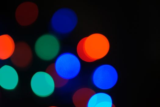 Multi-color blue holiday garland. Garland is blurred. Many big colorful round lights. Fully defocused photo. Blurred background and foreground. Holiday mood. New Year and Christmas is coming.